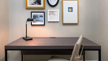 A desk with a chair, a framed picture, a clock, and a lamp.