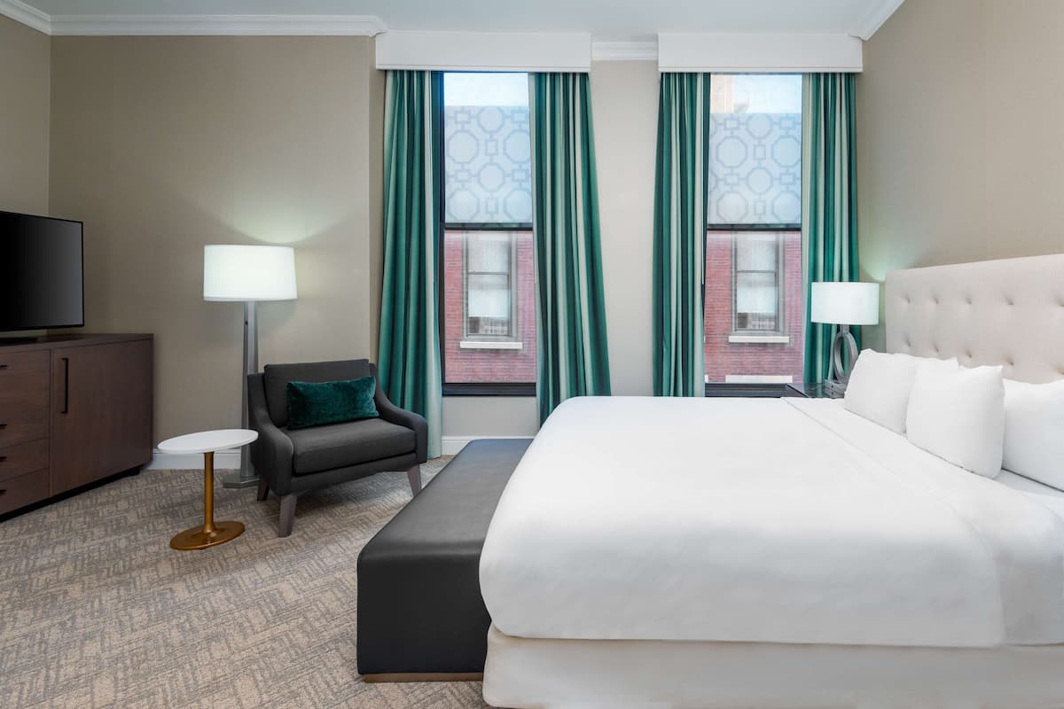 A hotel room with a large bed, a desk, a chair, a TV, and a window with curtains.