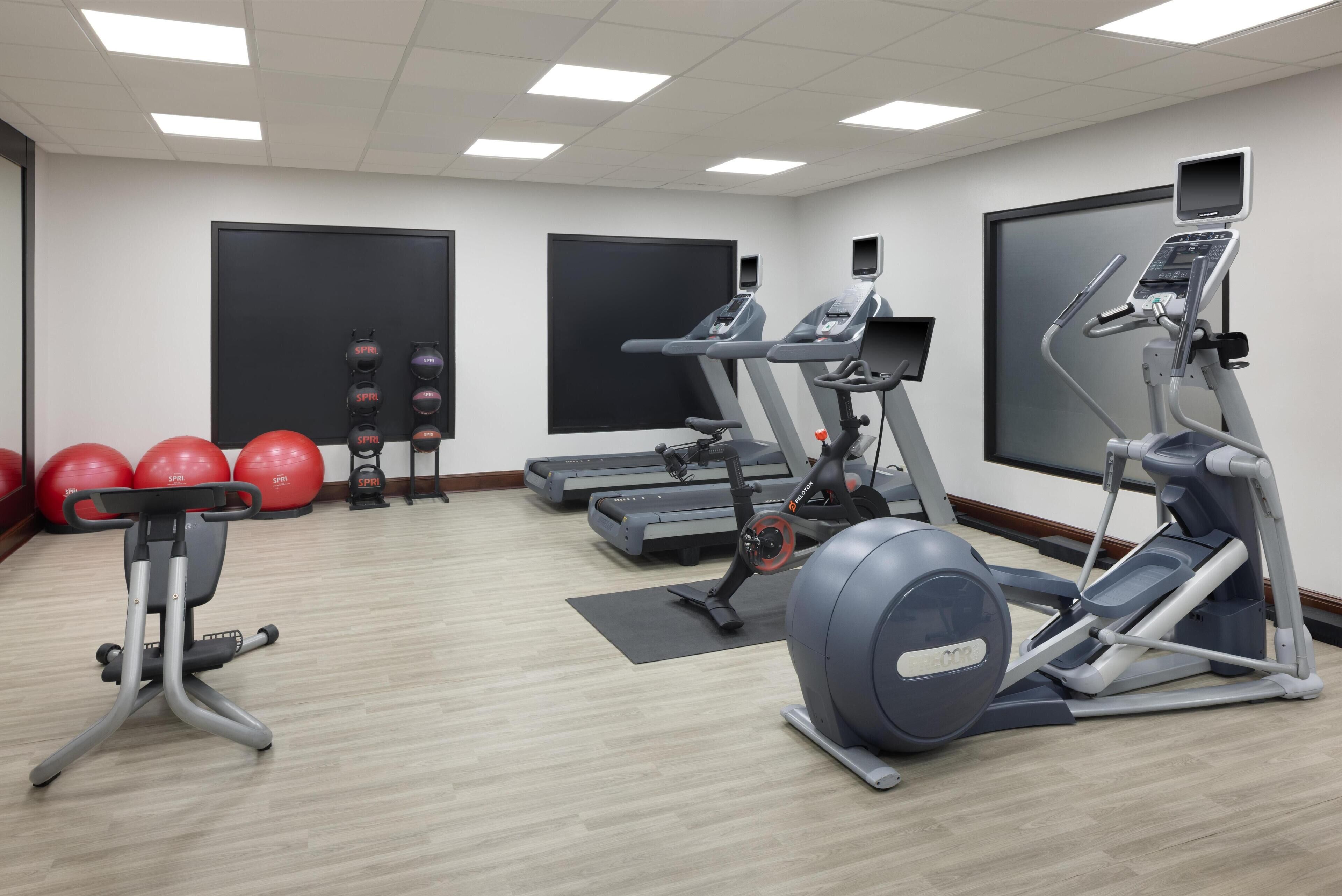 Un gimnasio con cintas de correr, elípticas y pelotas de ejercicio rojas.