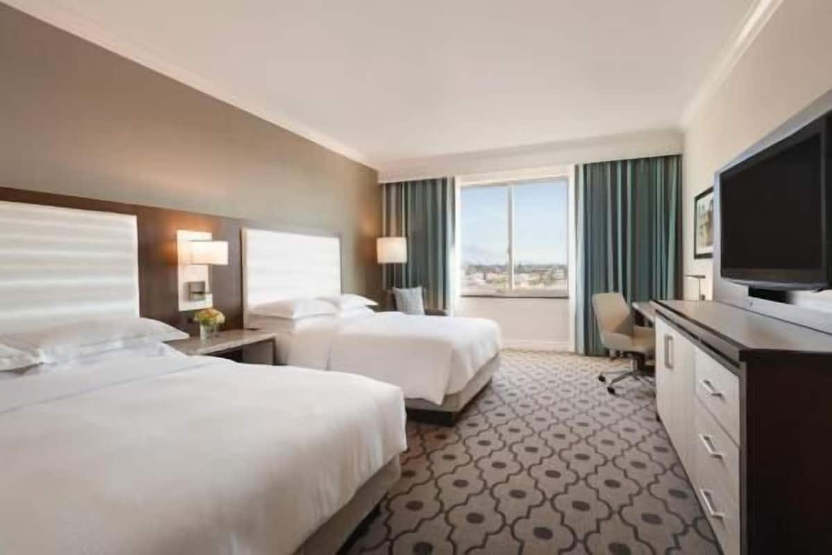 Une chambre d’hôtel avec deux lits, un bureau, une télévision et une vue sur la ville.