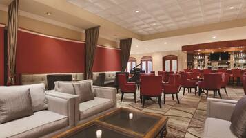 Un vestíbulo espacioso con una zona de bar, paredes de color rojo y beige, y diversas opciones de asientos, incluyendo sofás y sillones.