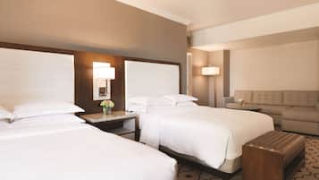 A hotel room with two beds, a sofa, a small table, and a nightstand with a lamp.