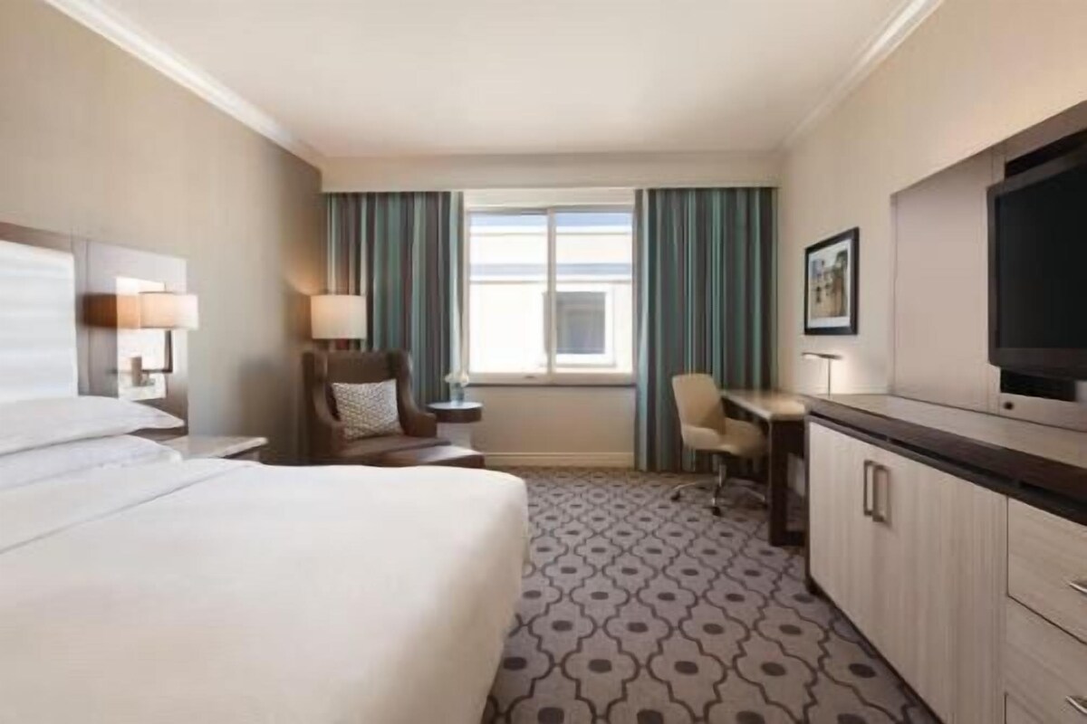 A hotel room with a bed, a desk, a chair, a television, and a window with curtains.