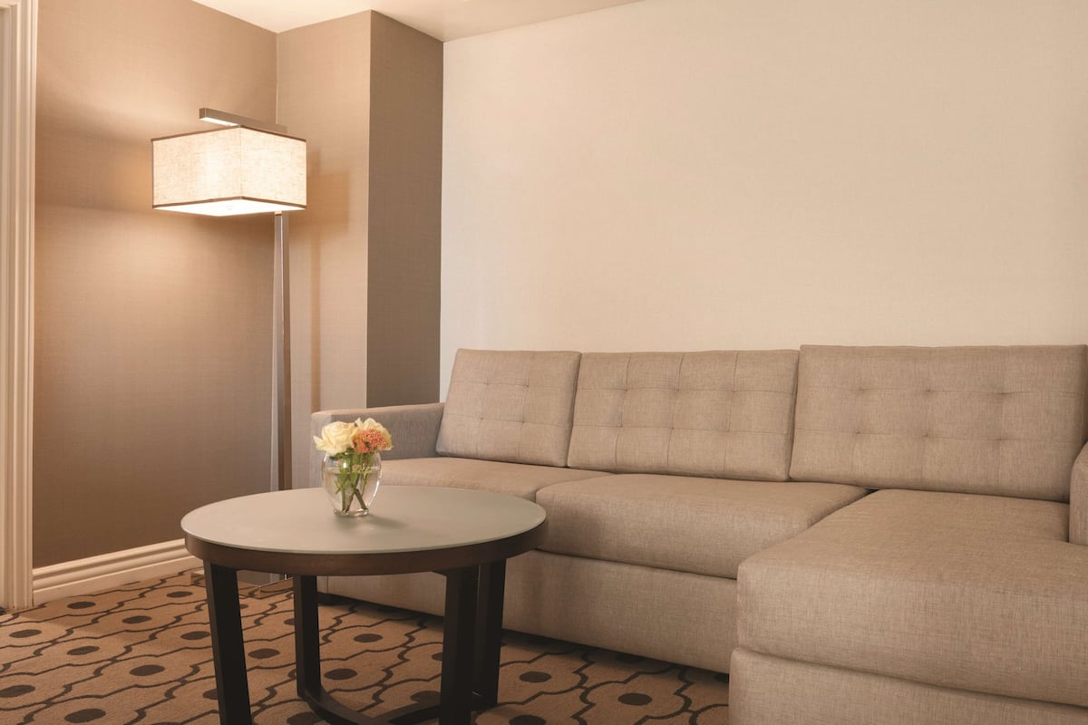 Un salon moderne avec un canapé d’angle beige, une table ronde ornée d’un vase de fleurs et un lampadaire.