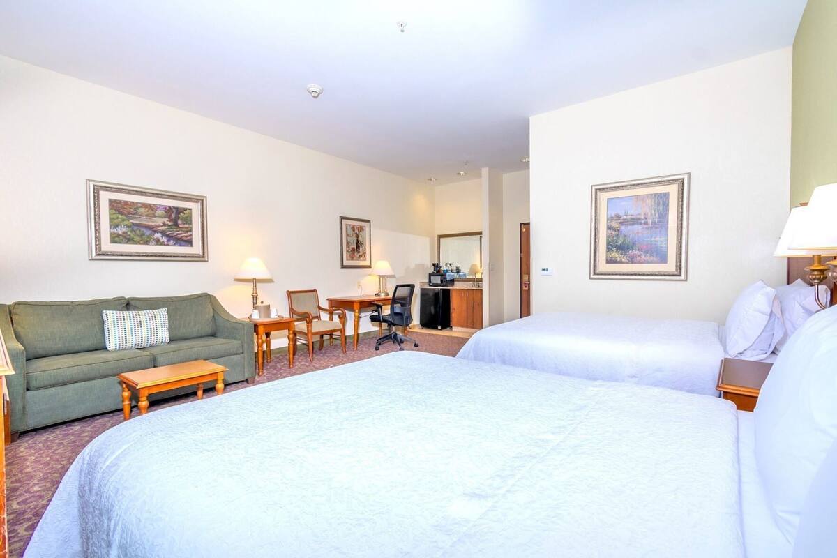 A hotel room with two beds, a sofa, a desk, and a chair.