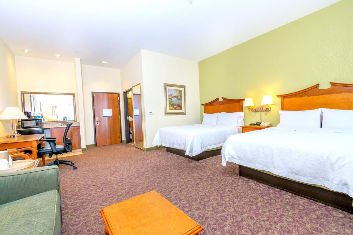 A hotel room with two beds, a desk with a chair, a TV, and a small table.