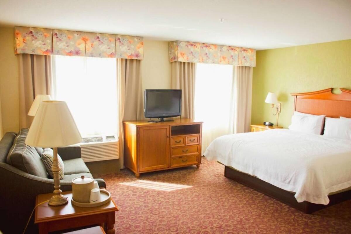 A hotel room with a bed, a television on a wooden cabinet, a sofa, and a lamp.