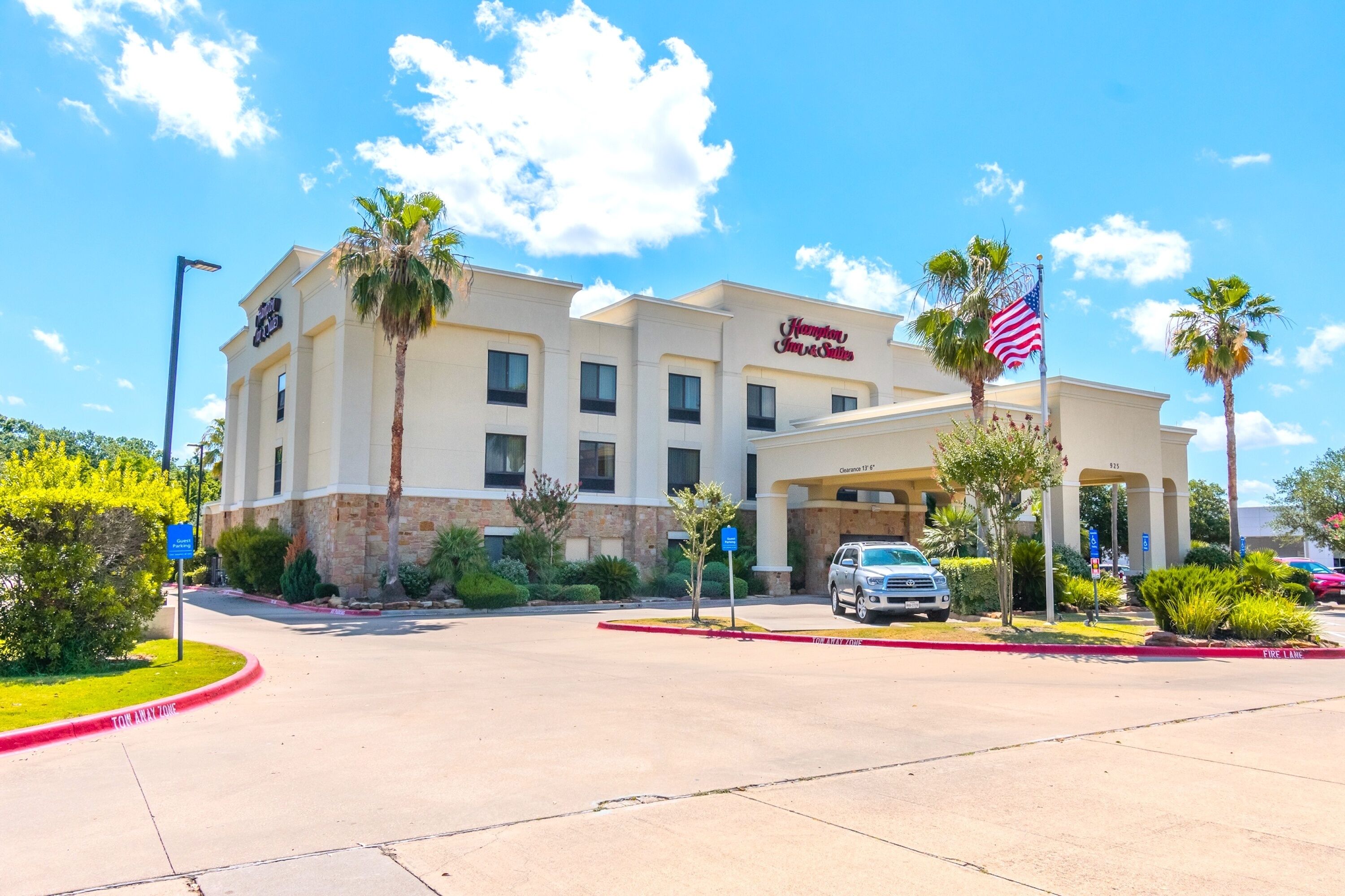 A Hampton Inn hotel with a two-story building, a parking lot, and an American flag.