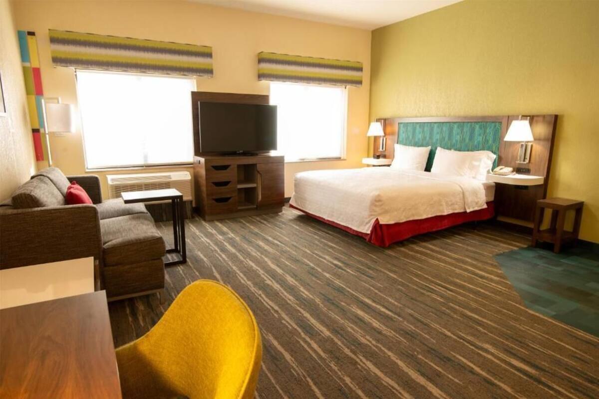A hotel room with a bed, a TV, a desk, a chair, and a window.