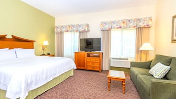 A hotel room with a large bed, a wooden dresser, a television, a sofa, and two lamps.