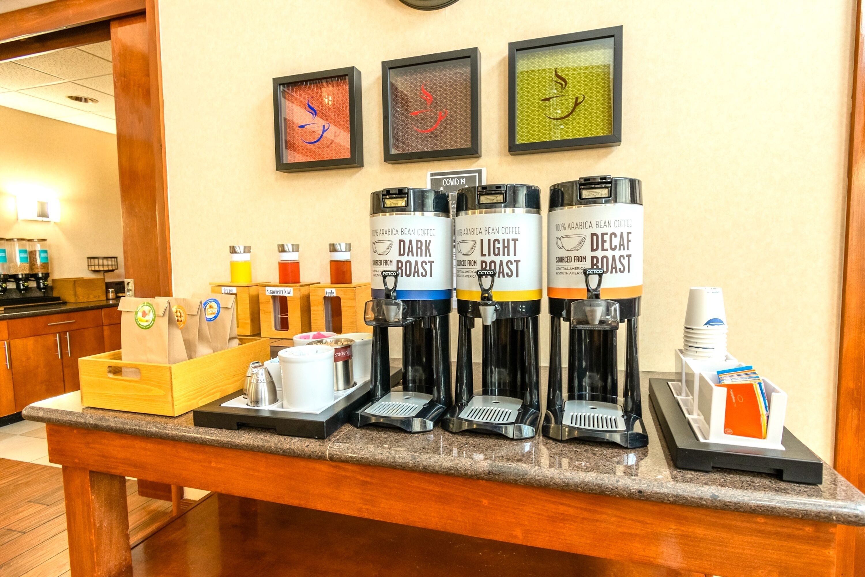 Una estación de café con cuatro dispensadores de café, etiquetados como: tostado oscuro, tostado claro y descafeinado. Hay bolsas de papel y una cafetera sobre el mostrador.