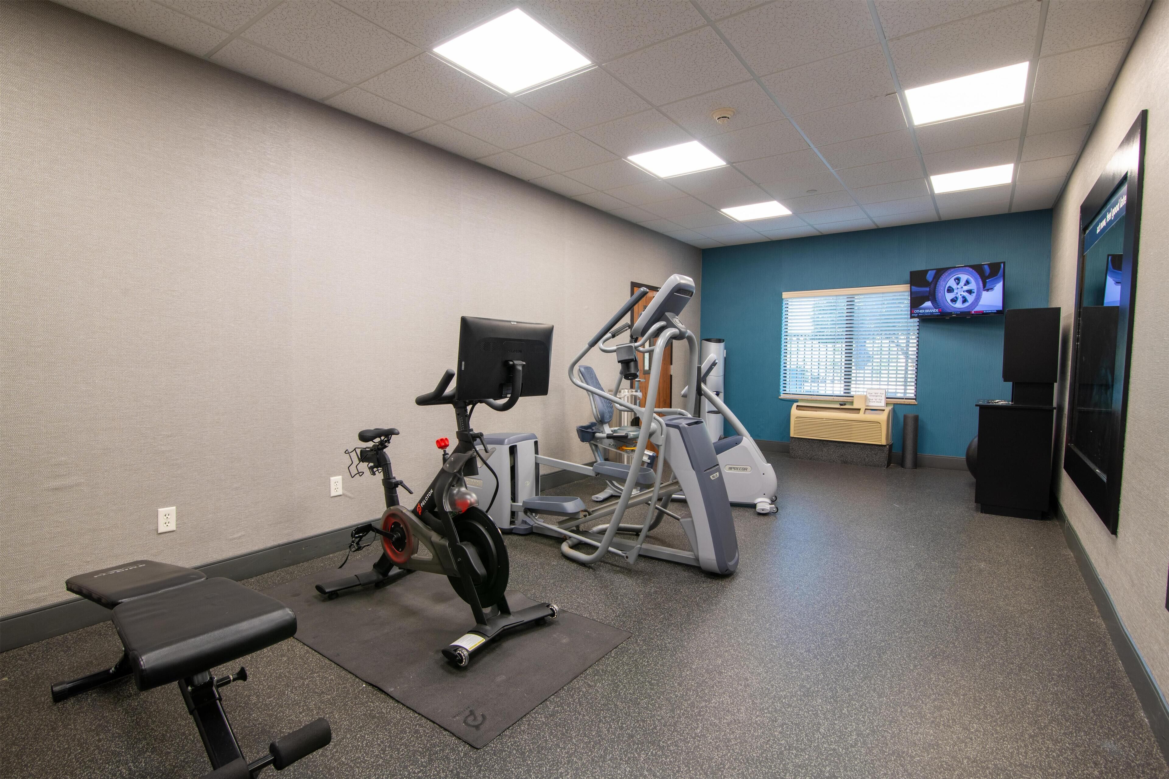 Un gimnasio con equipo de ejercicio, una banca y un televisor en la pared.