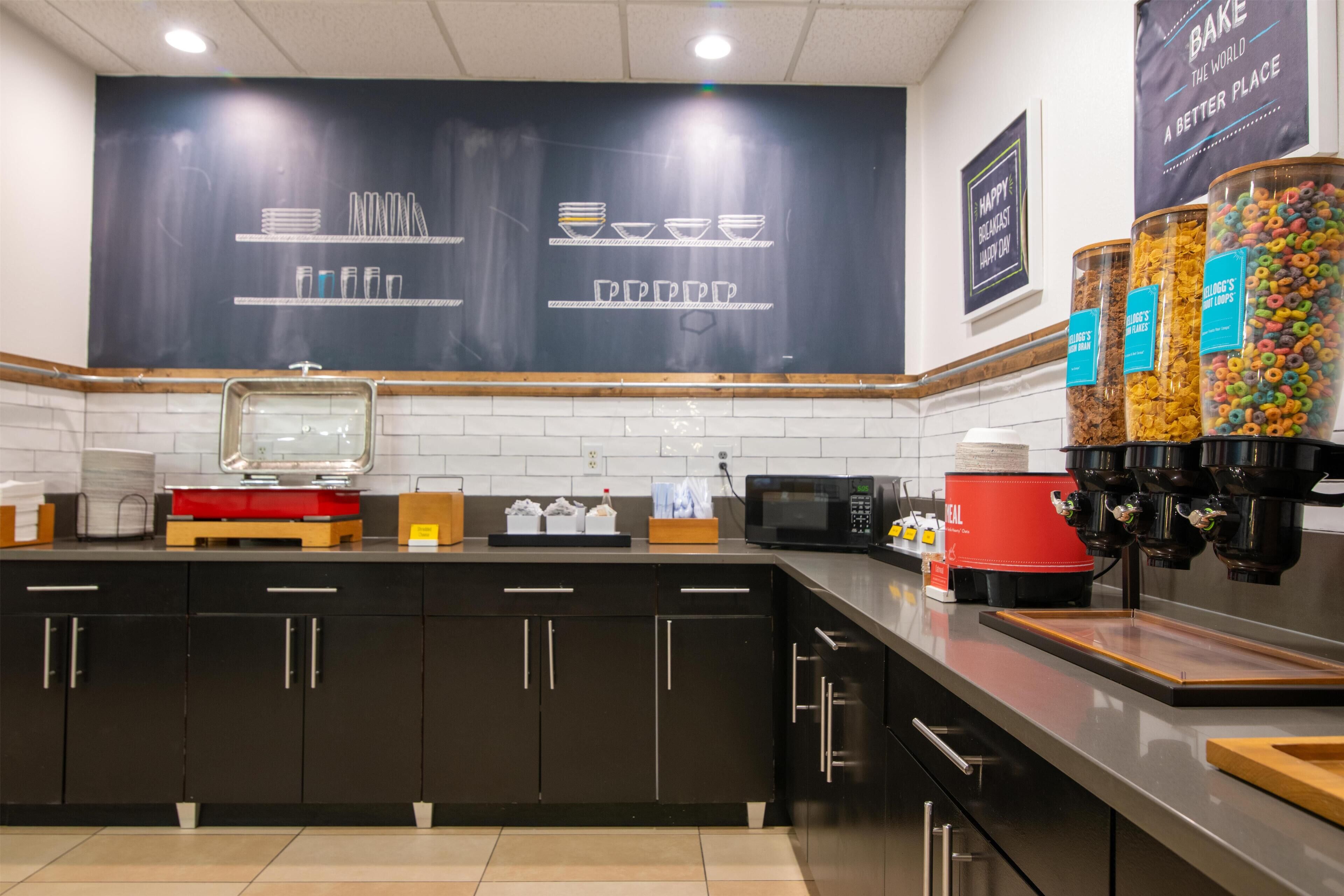 A modern kitchen with dark cabinetry, a microwave, a coffee machine, and a chalkboard wall with utensils and bowls.