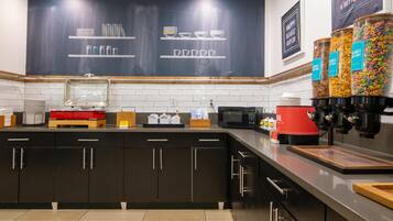 A modern kitchen with dark cabinetry, a microwave, a coffee machine, and a chalkboard wall with utensils and bowls.