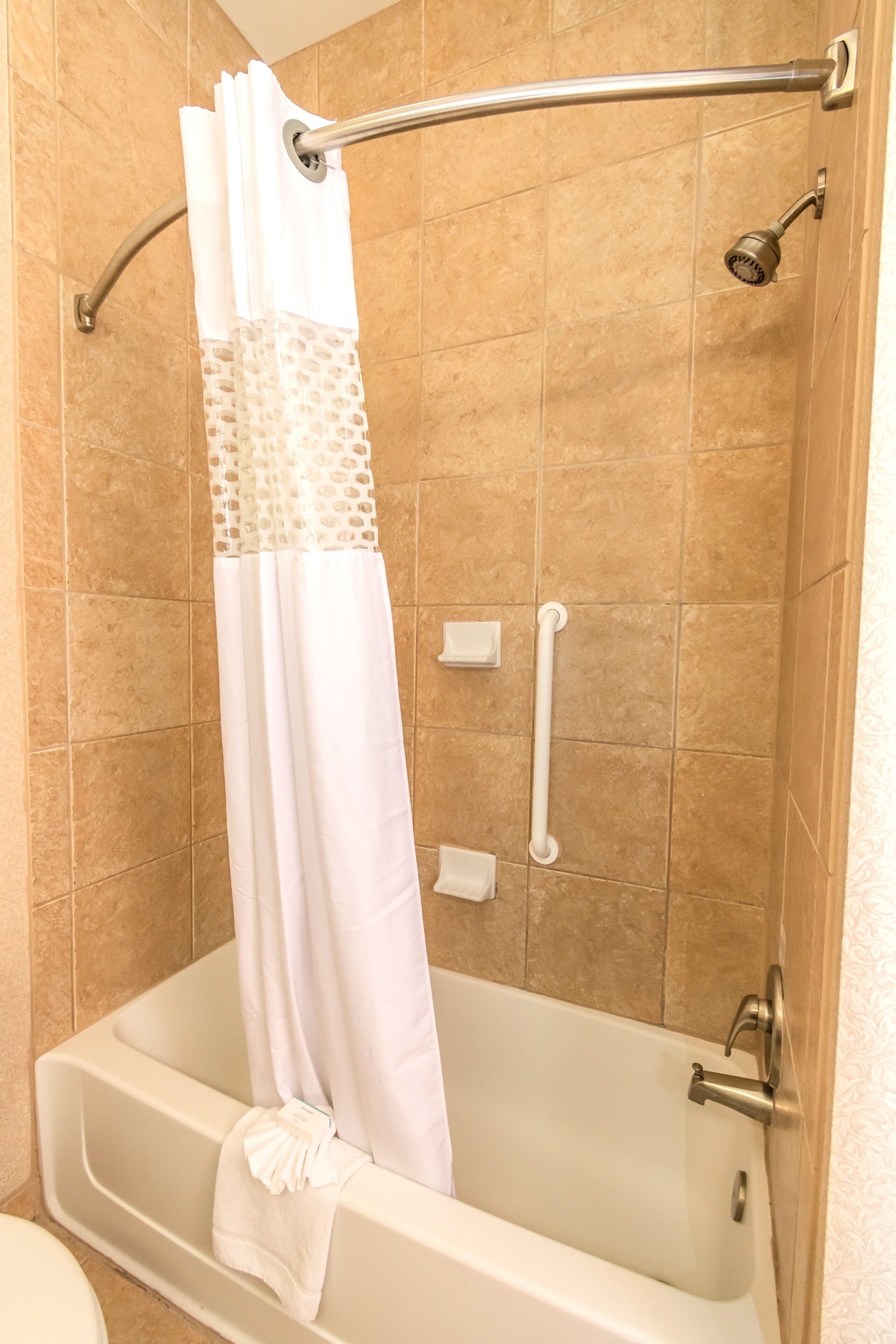A bathtub with a shower curtain, grab bars, and a towel rack.