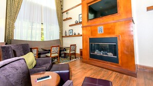 Un salon doté d’une cheminée, d’un téléviseur fixé à un mur en bois et d’un coin repas avec des chaises et une table.