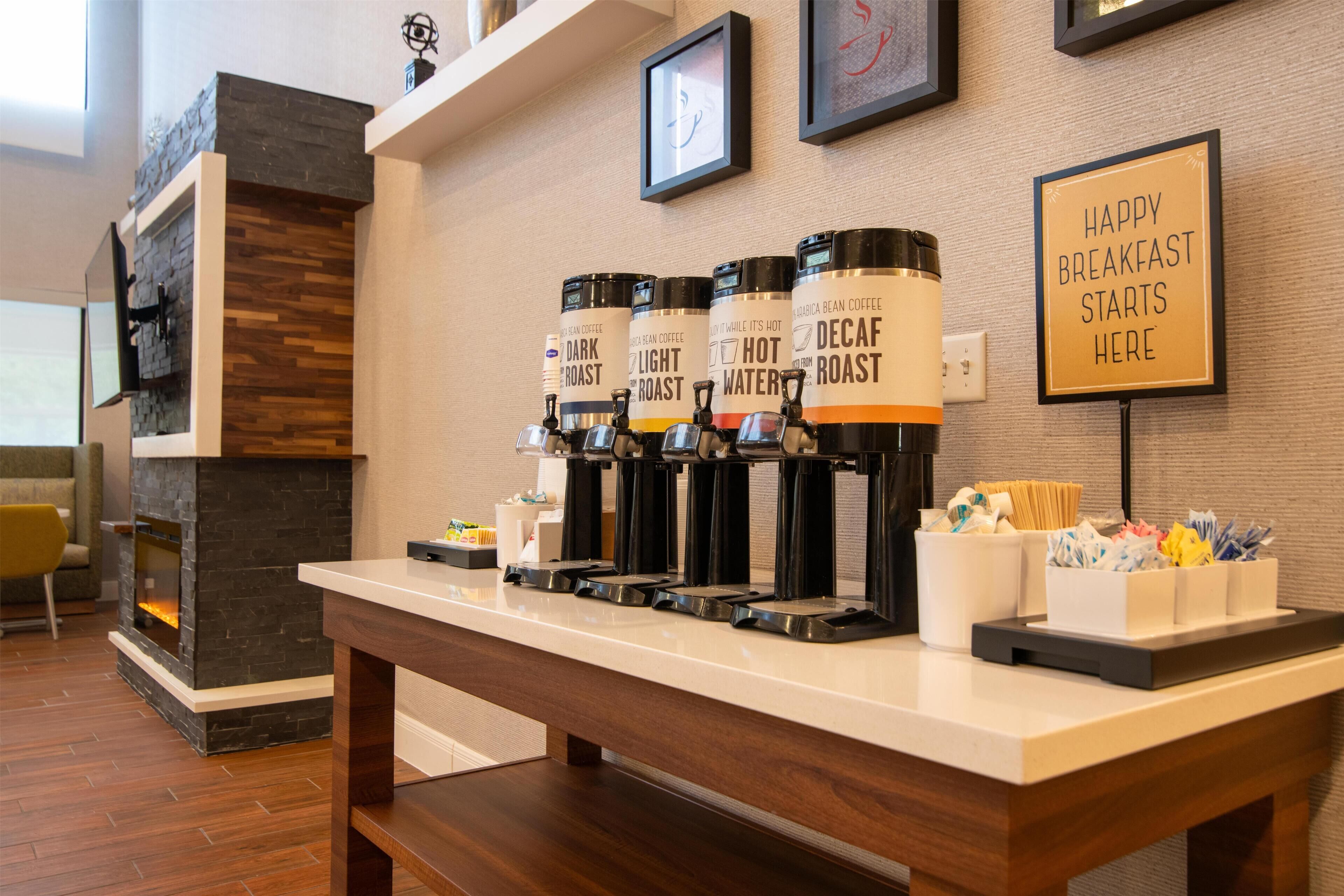 Un comptoir pour le petit-déjeuner est équipé de distributeurs de café avec les mentions suivantes : « Mélange corsé », « Mélange léger », « Eau chaude » et « Mélange décaféiné ». Un panneau est affiché sur le mur avec l’inscription : « Un petit-déjeuner réussi commence ici ».