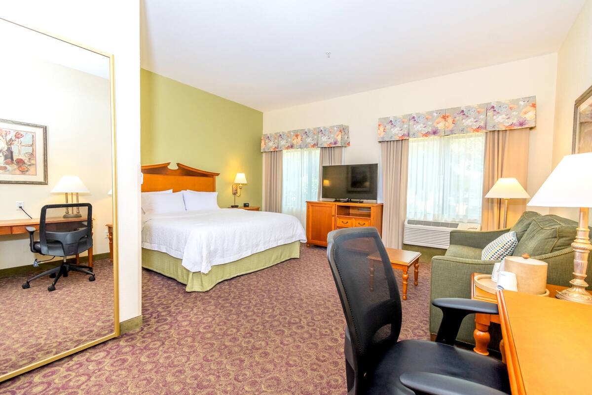 A hotel room with a bed, a desk with a chair, a sofa, a television, and a mirror.