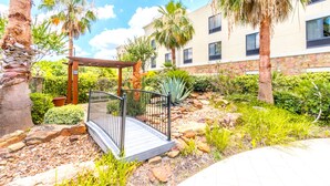 Un espace extérieur aménagé avec une pergola en bois, des palmiers et un bâtiment doté de nombreuses fenêtres en arrière-plan.