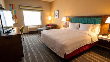 Habitación de hotel con una cama grande, un escritorio con ordenador, una silla y una ventana con persianas.