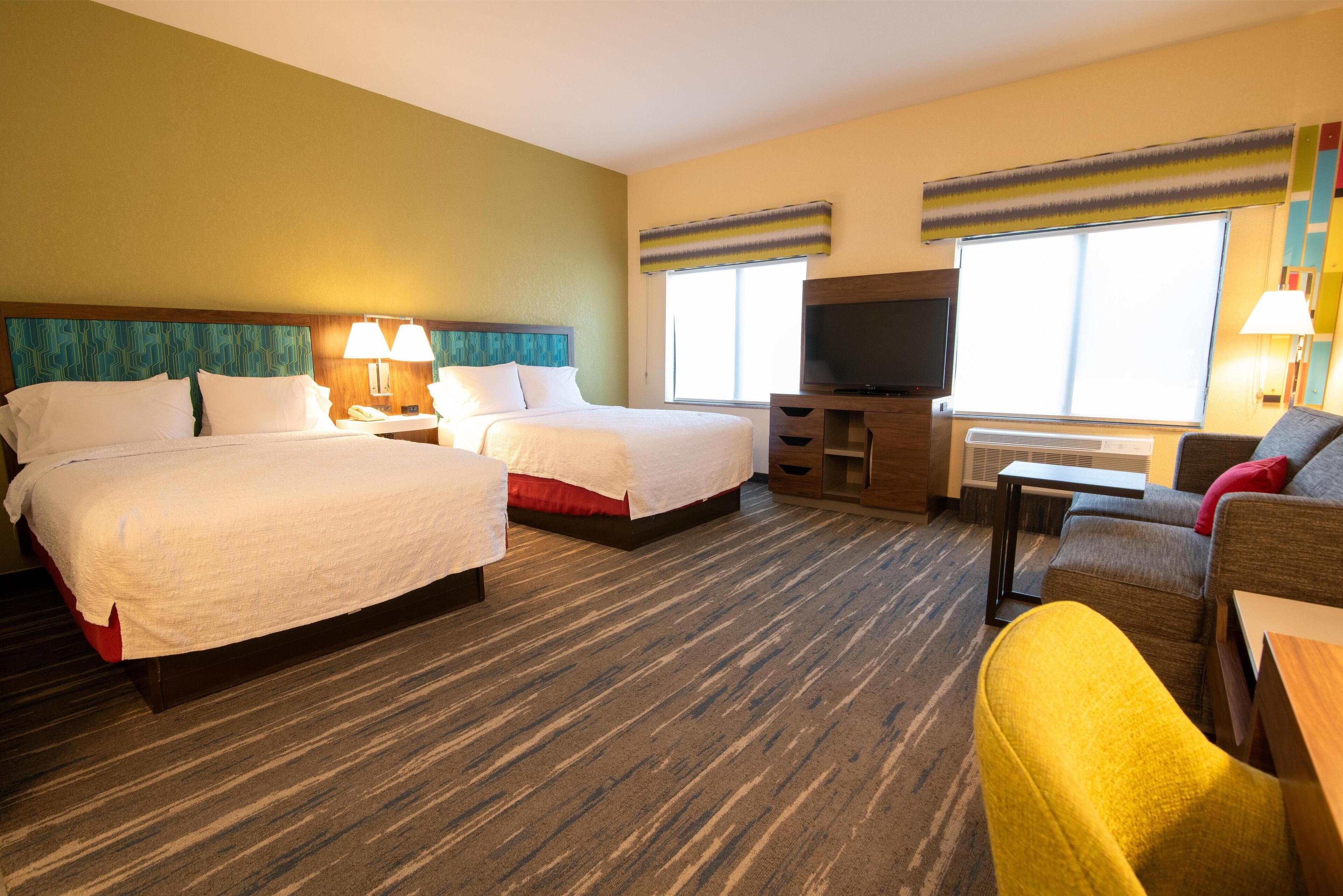 A hotel room with two beds, a TV, a desk, and a sofa.