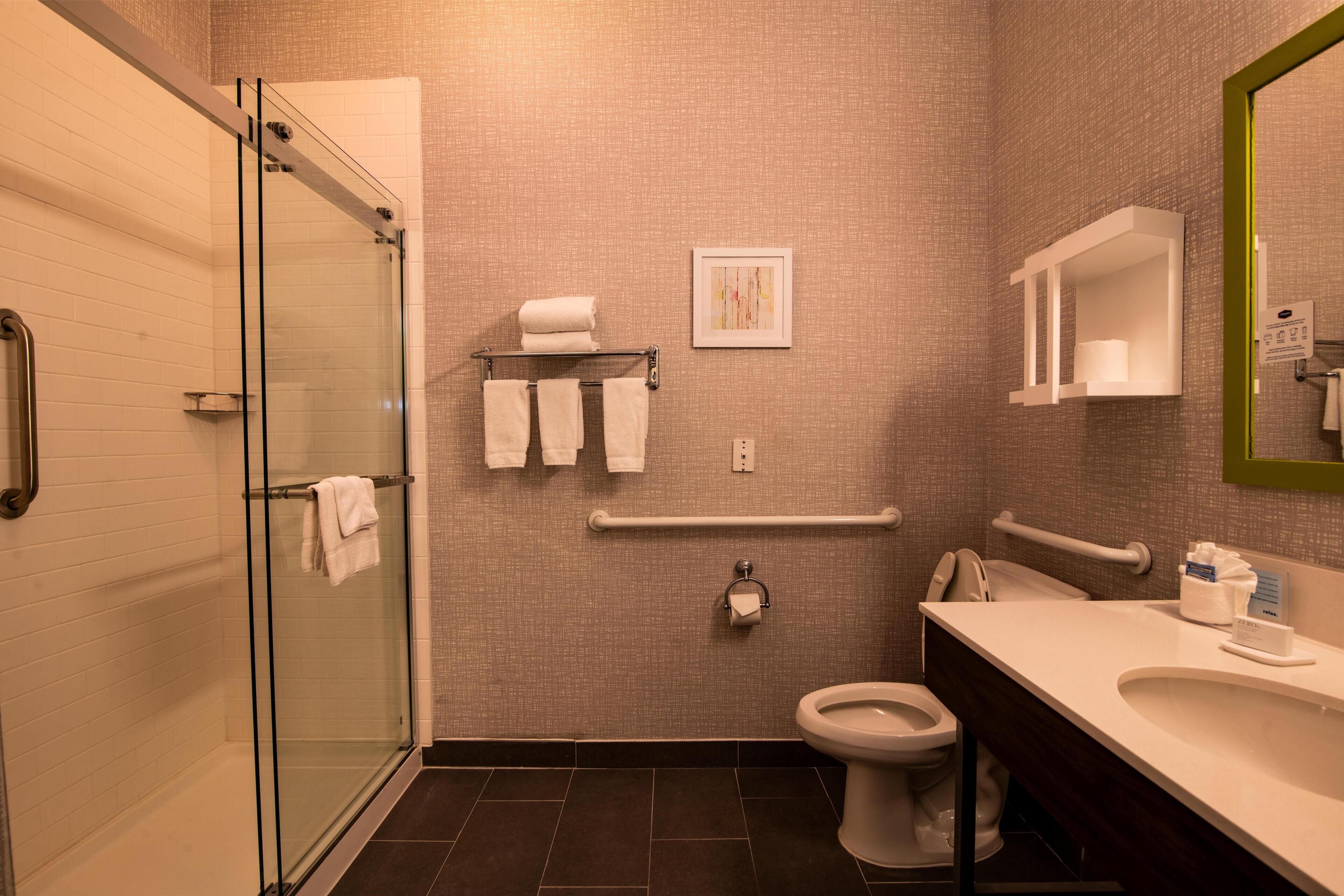 Un baño moderno con cabina de ducha de vidrio, inodoro blanco y tocador con espejo.