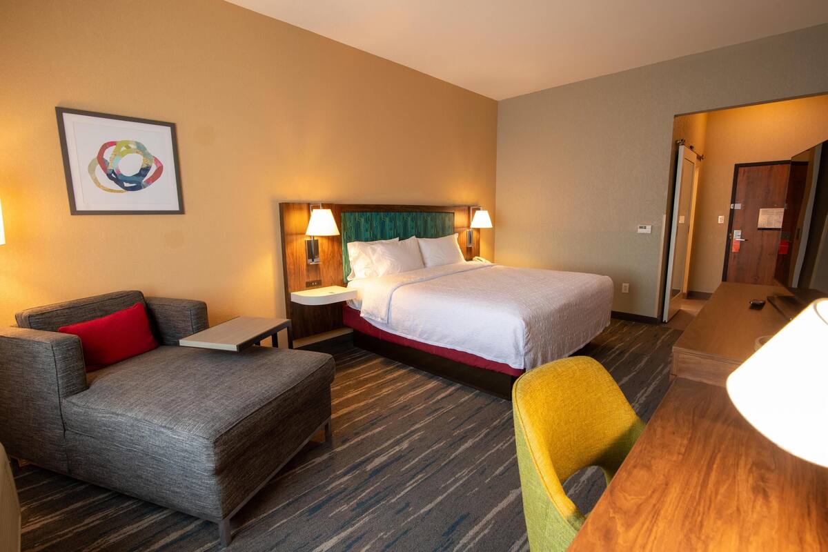 A hotel room with a bed, a sofa, a chair, a small table, and a desk.