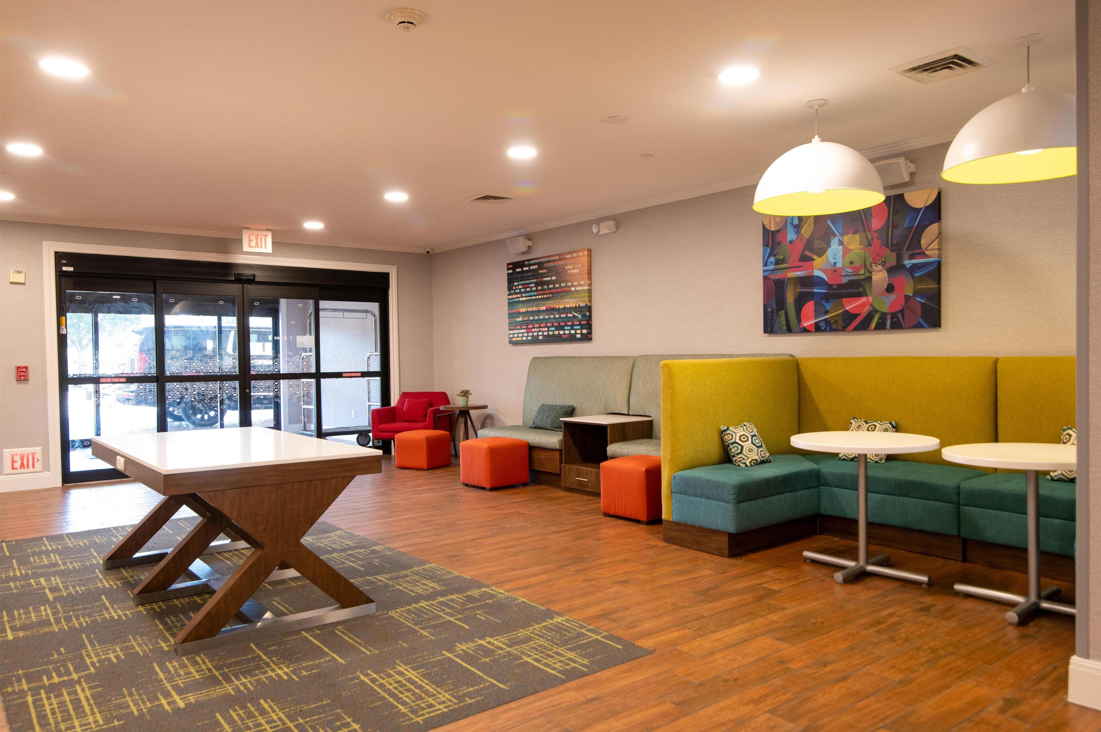 A modern lounge area with a wooden table, colorful seating, and pendant lighting.