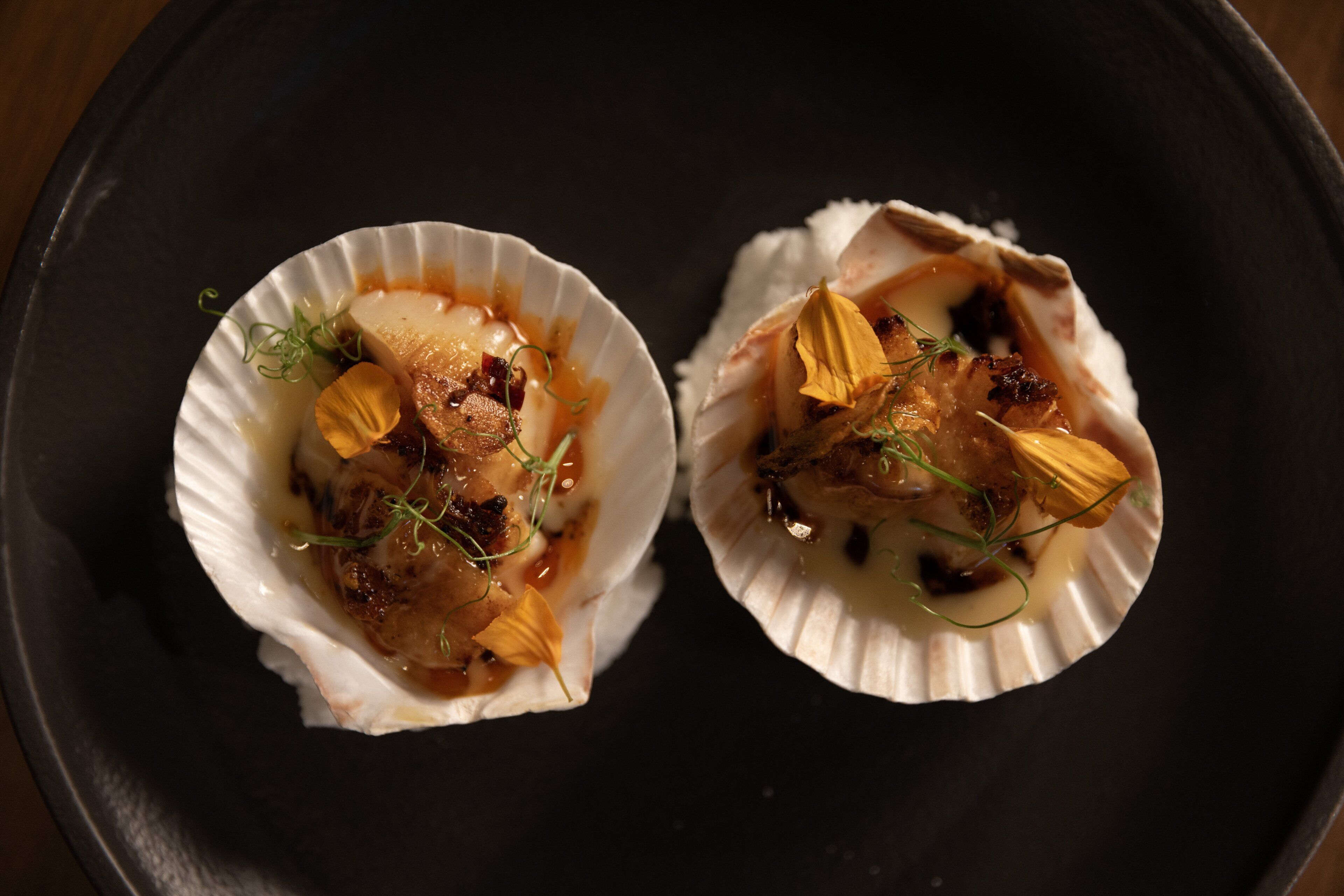 Deux coquilles Saint-Jacques servies dans leurs coquilles, accompagnées d’une garniture.