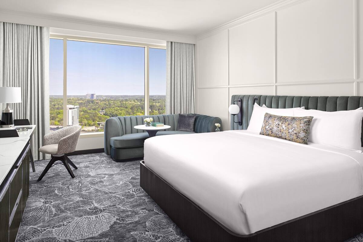 A hotel room with a large bed, a desk, a chair, and a view of the city.