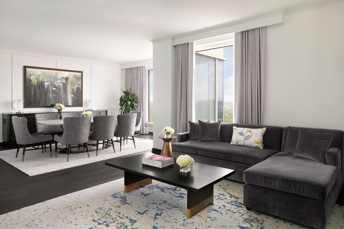 A modern living room with a dark grey sectional sofa, a round coffee table, and a dining area with grey upholstered chairs.