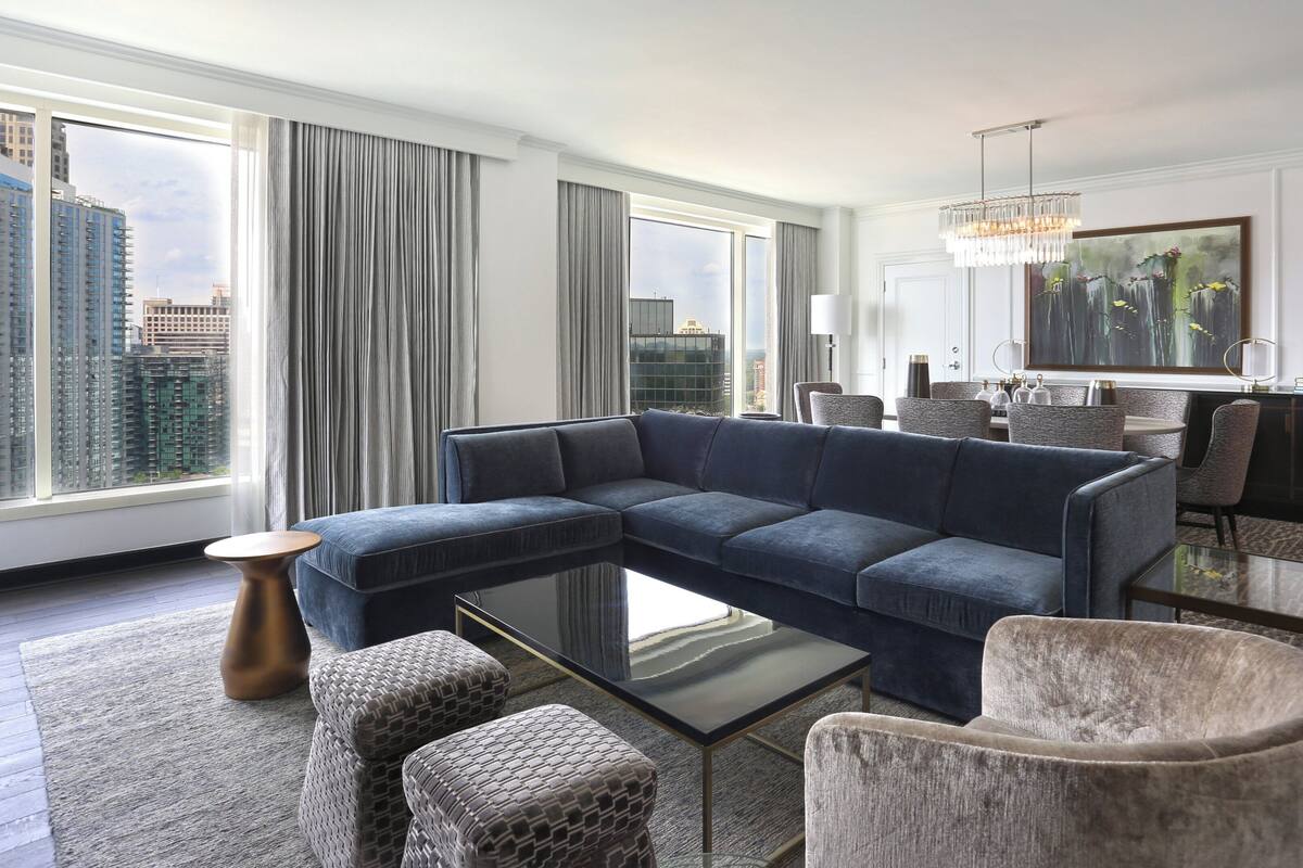 A modern living room with a sectional sofa, a glass coffee table, and a dining area with a chandelier.