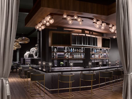 A modern bar area with a central island, bar stools, and a variety of bottles and glasses on shelves.