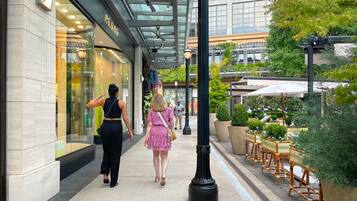 A walkway with a glass storefront, outdoor seating, and potted plants.