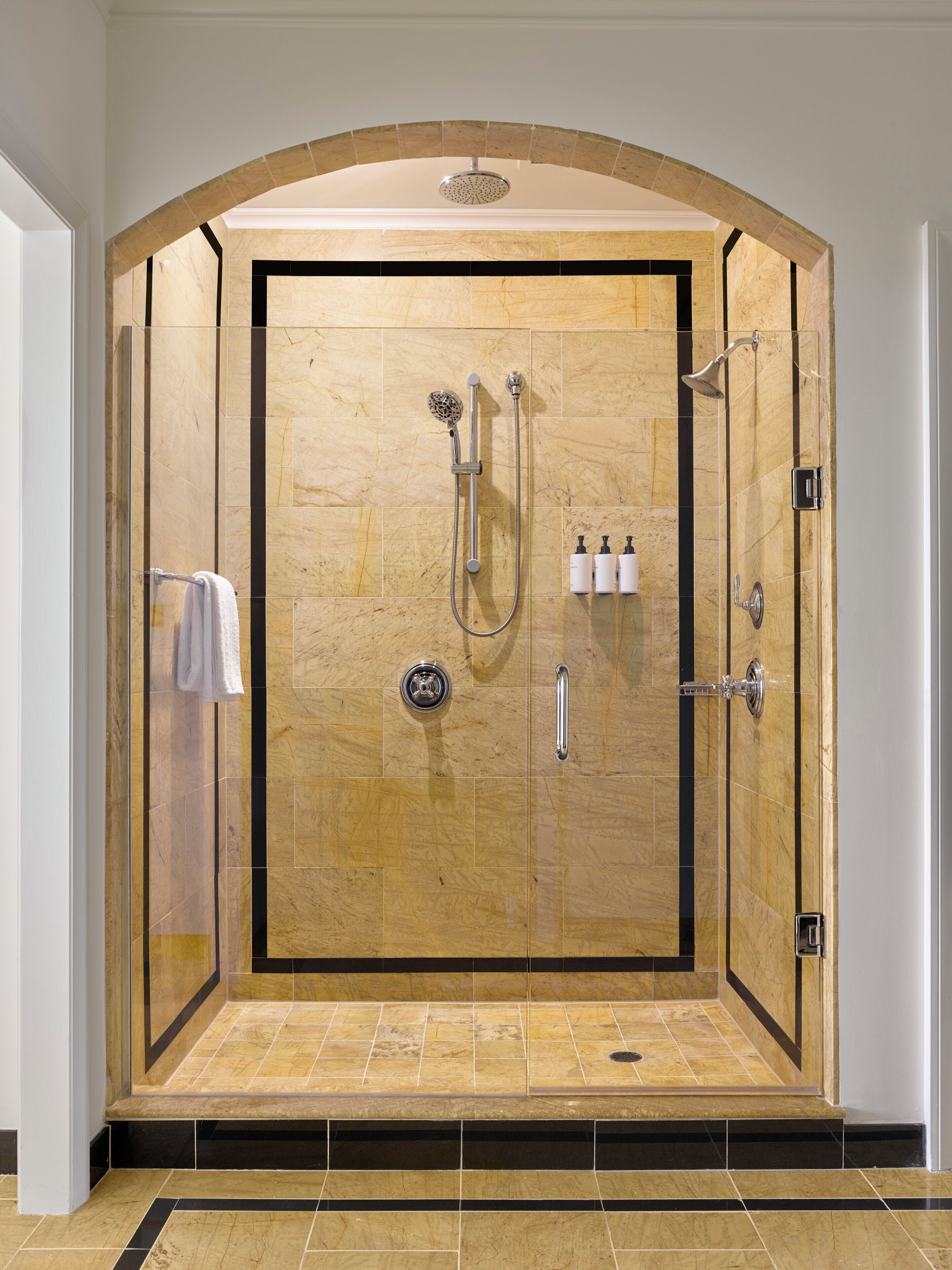A walk-in shower with a glass door, a handheld showerhead, a wall-mounted faucet, and a handheld showerhead.