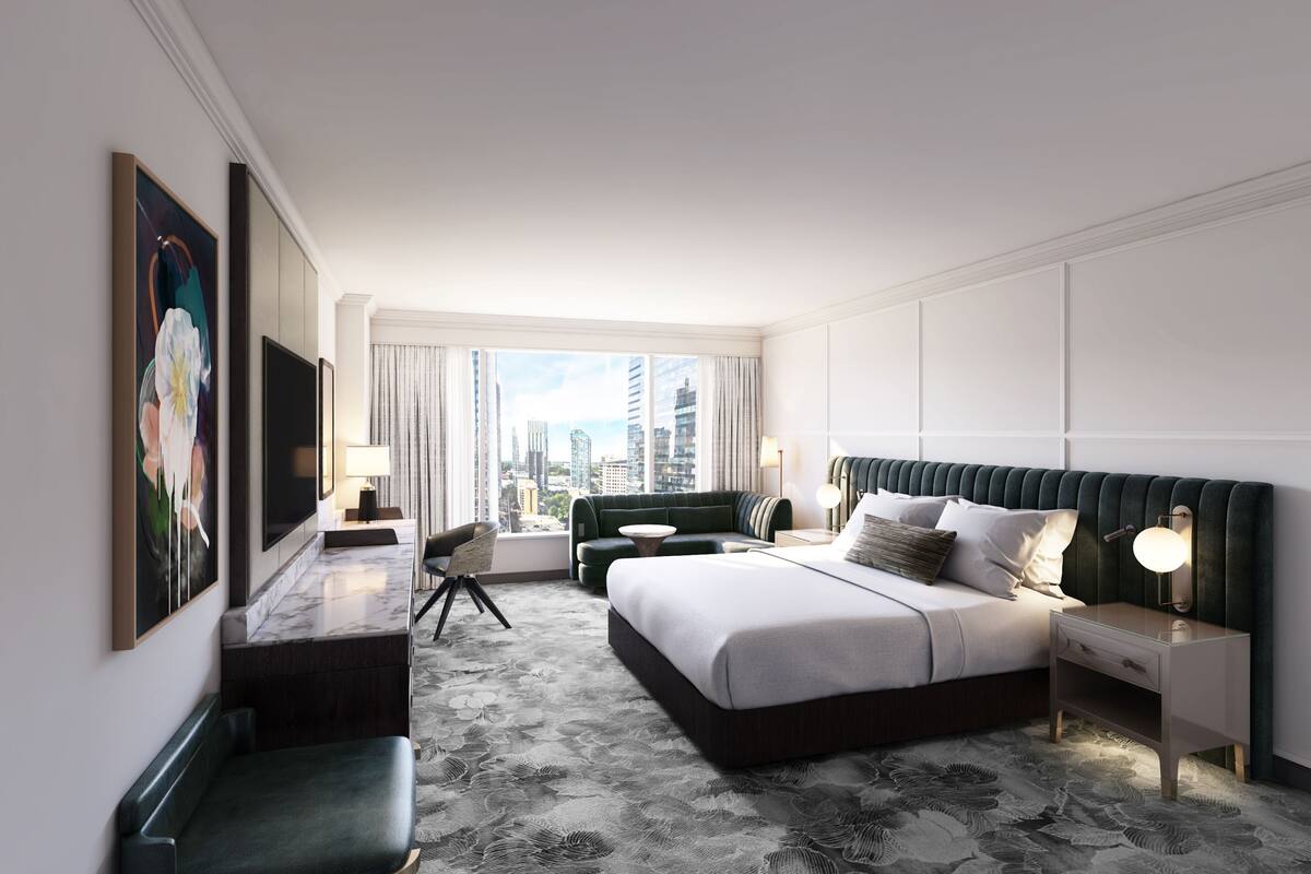 A modern hotel room with a large bed, a desk, a chair, and a view of the city skyline.