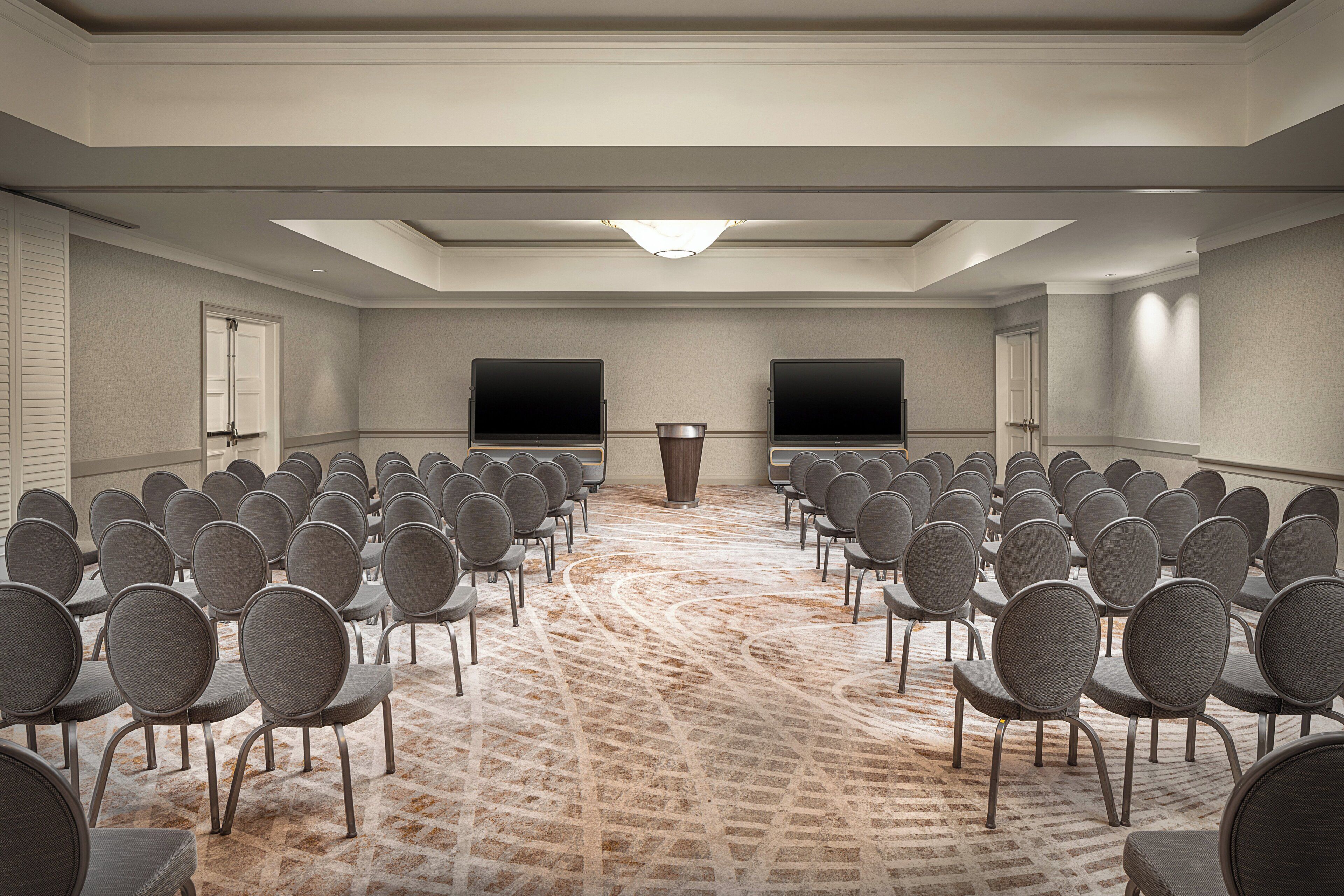A conference room with rows of chairs, a podium, and two large screens.