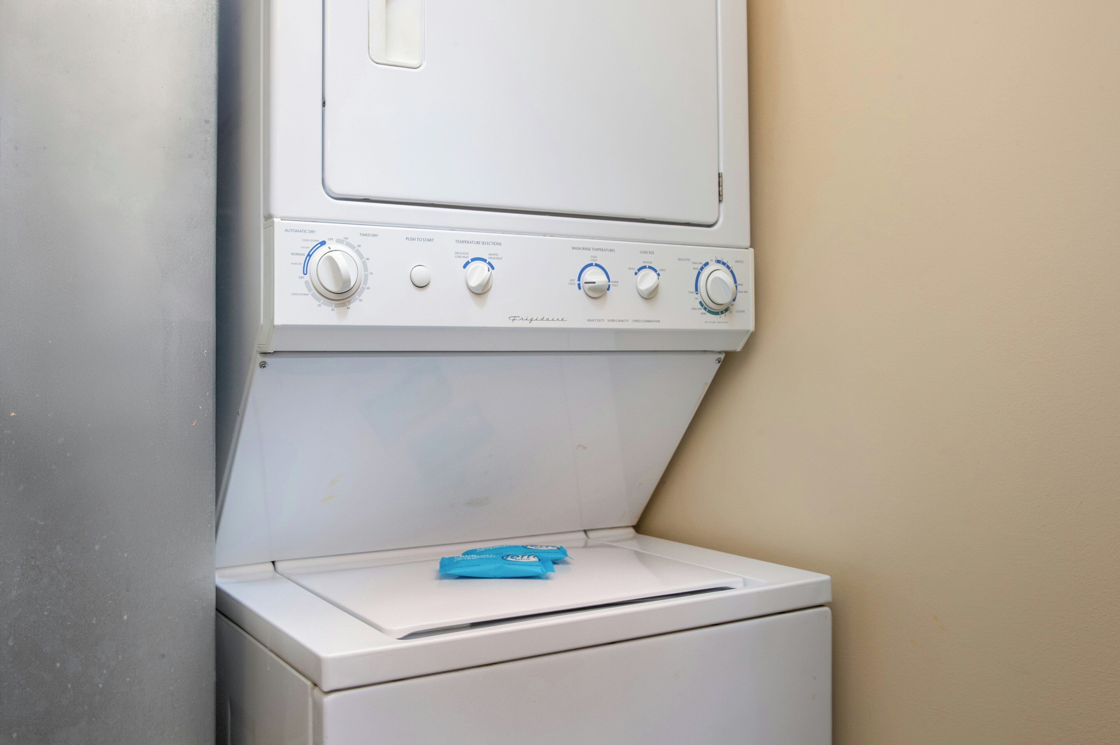 A front-loading washing machine with control knobs and a detergent packet on the door.