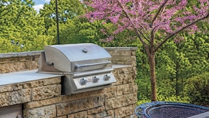 A stone barbecue grill with a control panel, set against a backdrop of trees and a clear sky. - WorldMark Galena (Hanover)
