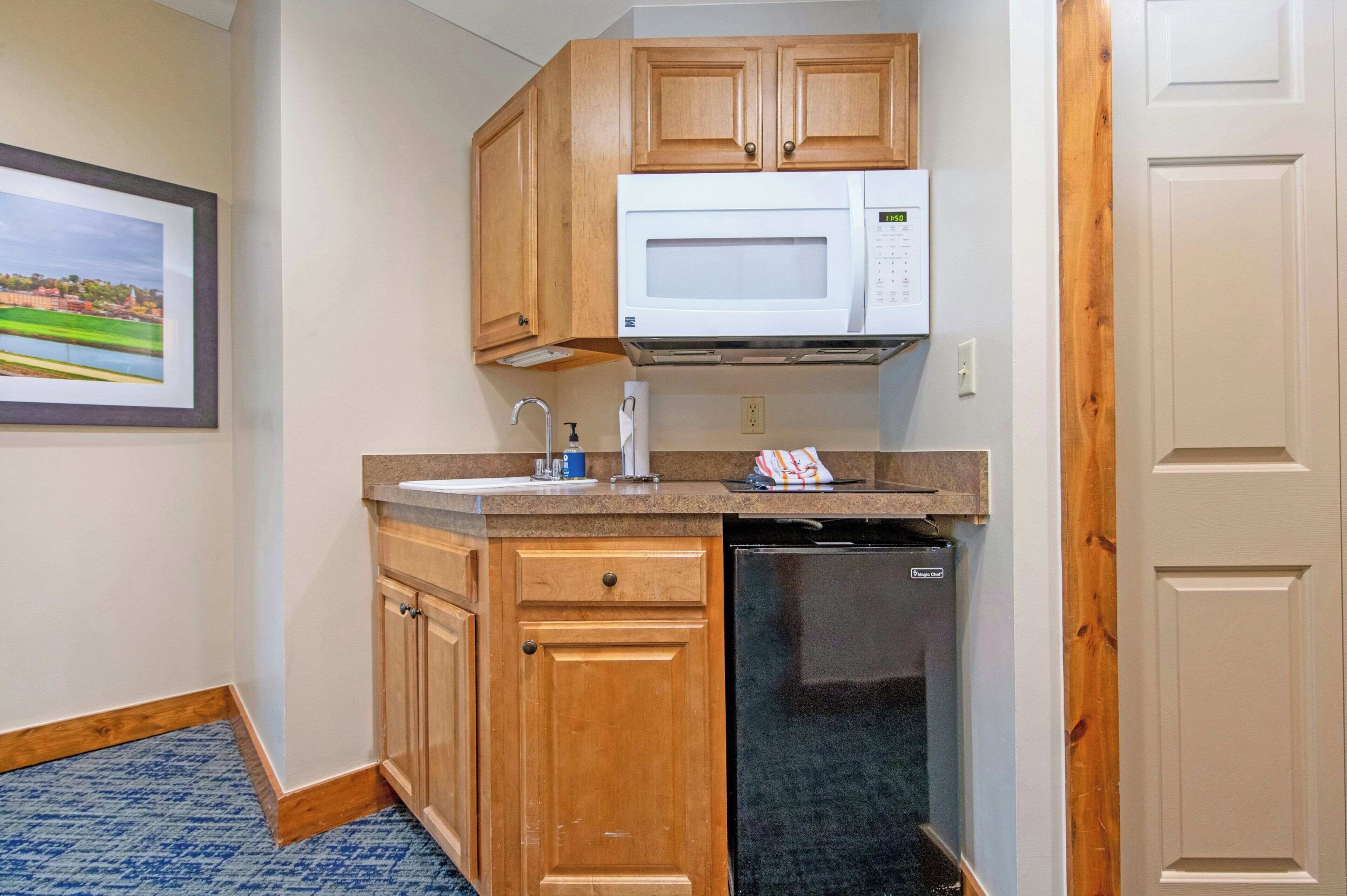 A compact kitchen with wooden cabinets, a built-in microwave, a sink, and a dishwasher.