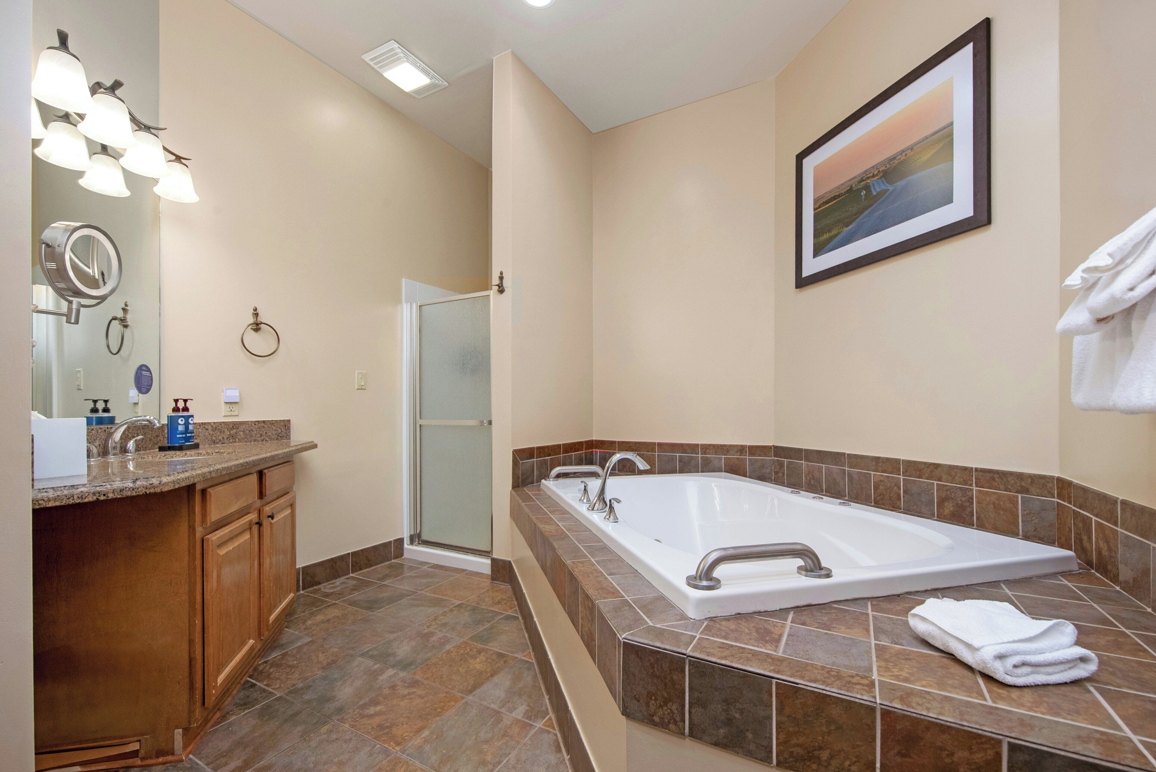 A bathroom with a large bathtub, a vanity with a mirror, and a shower area.