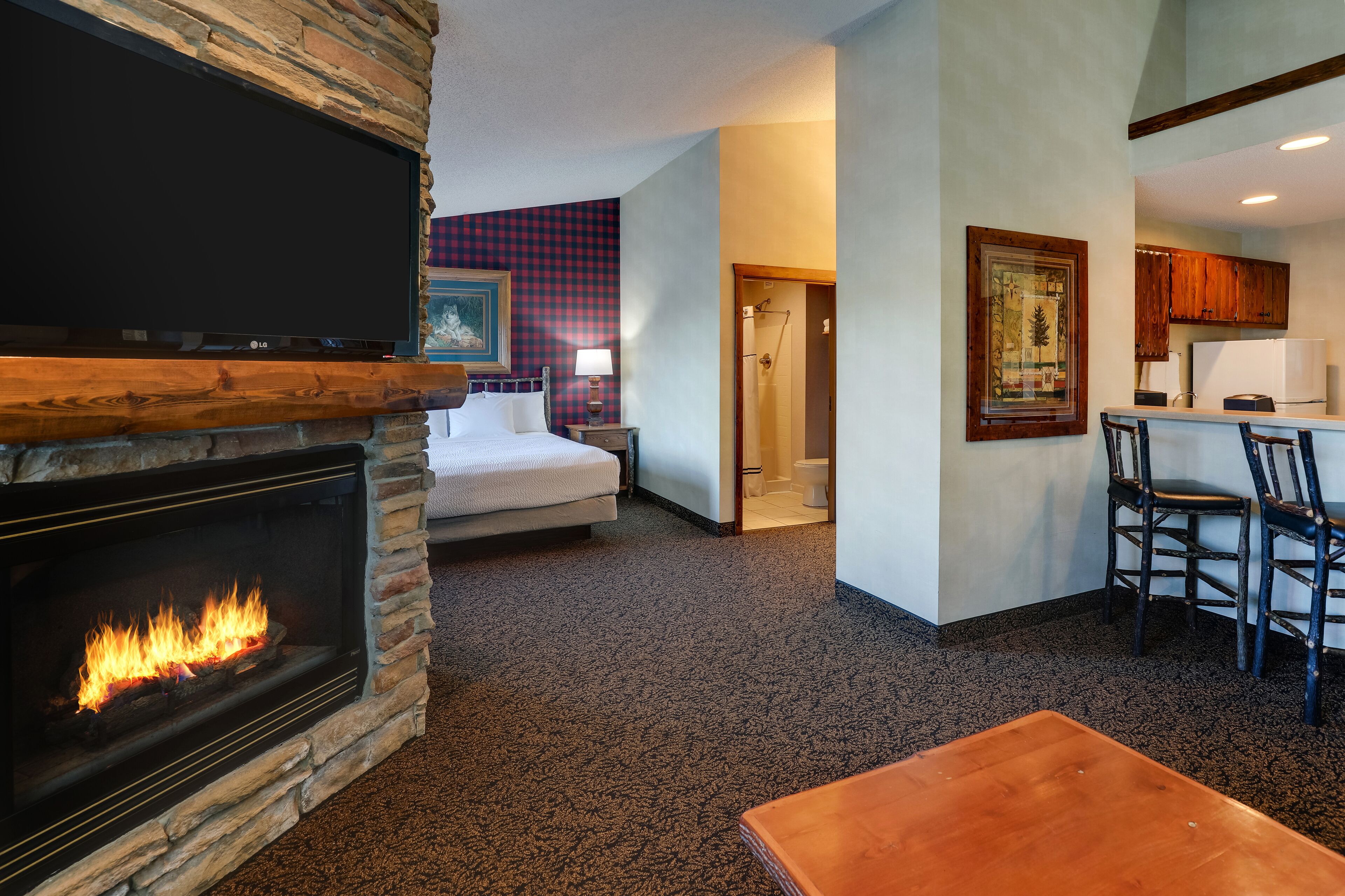A room with a fireplace, a bed, a dining area with chairs, and a kitchen area with cabinets.