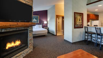 A room with a fireplace, a bed, a dining area with chairs, and a kitchen area with cabinets.