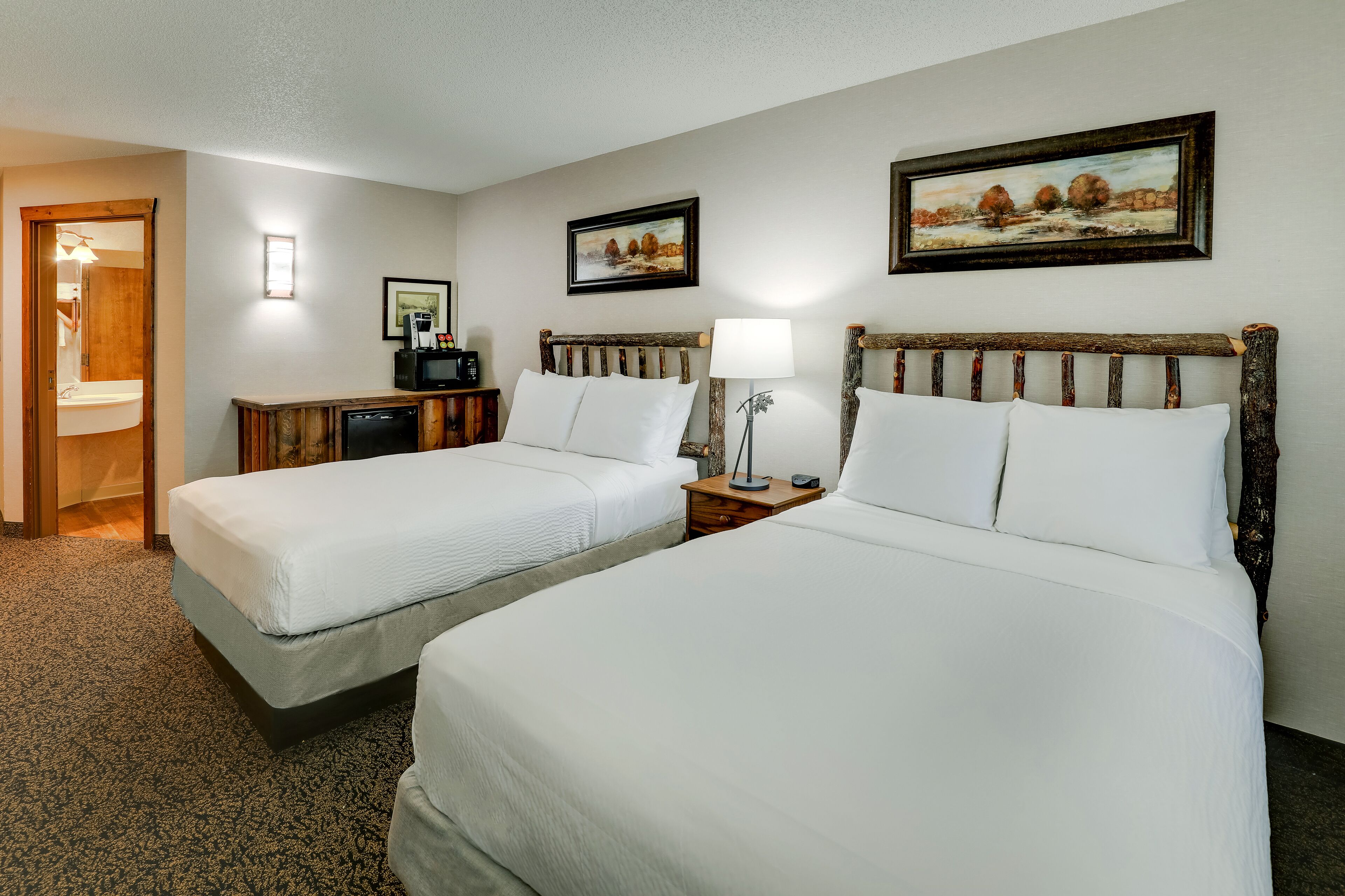 A hotel room with two beds, a desk, a chair, a lamp, and a painting on the wall.