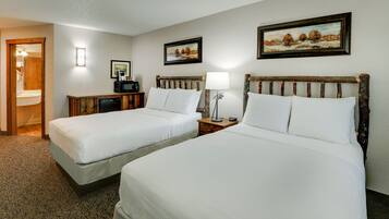 A hotel room with two beds, a desk, a chair, a lamp, and a painting on the wall.