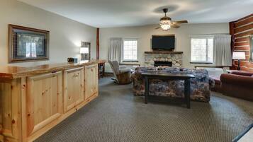 A spacious living room with a stone fireplace, a wooden bar, and a television mounted above it.