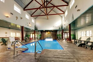 Una piscina interior con cascada, rodeada de sillas Adirondack y una terraza de madera.
