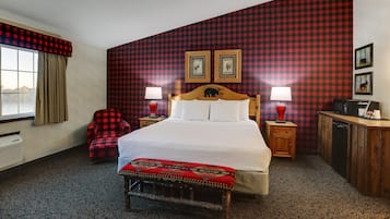 Een hotelkamer met een groot bed, twee nachtkastjes met lampen, een houten bankje, een rode geruite fauteuil en een geruite wand.