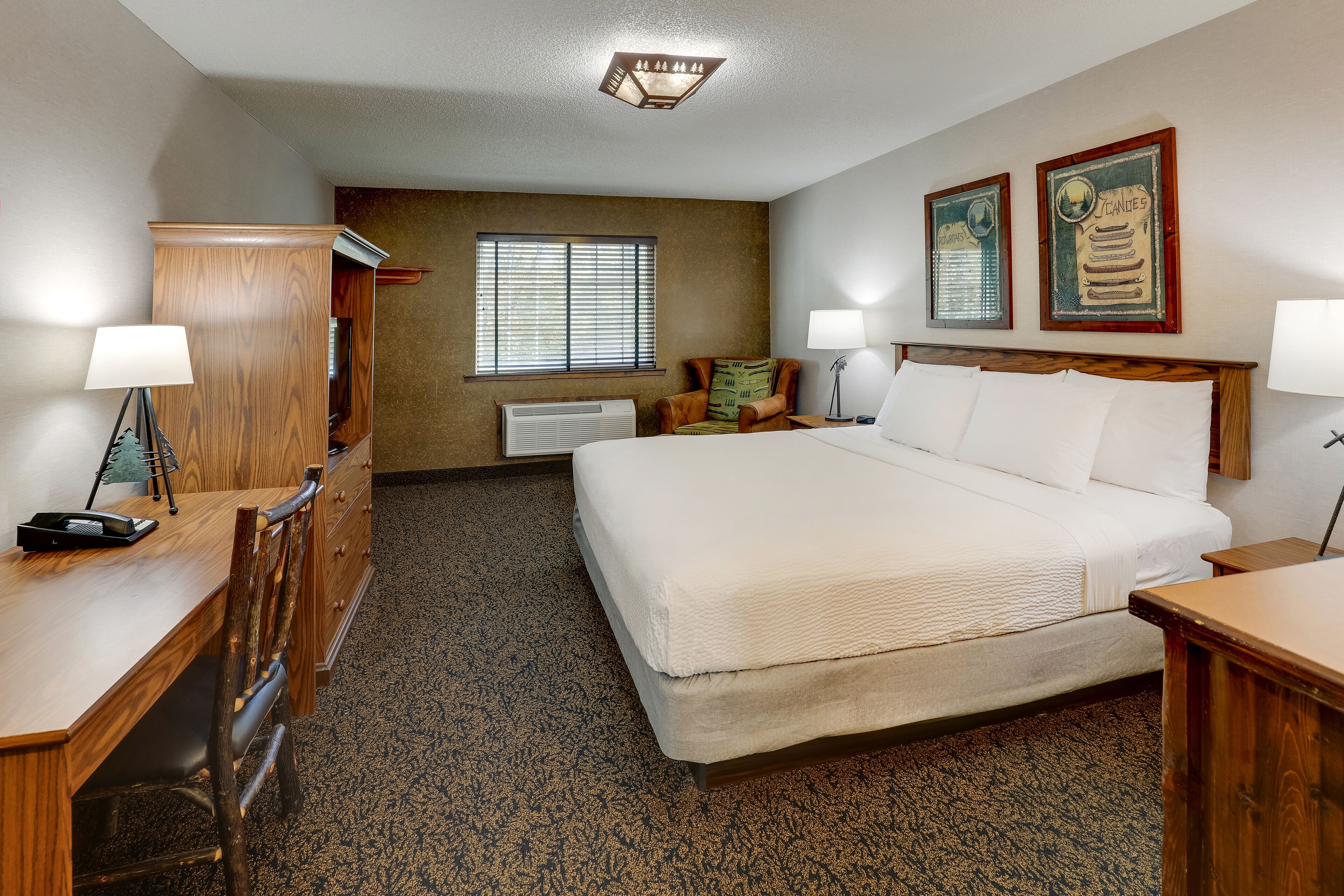 A hotel room with a large bed, a wooden desk, a chair, a dresser, and two wall-mounted lamps.