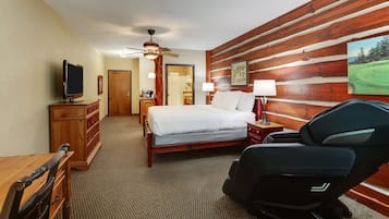 A hotel room with a bed, a desk, a chair, a television, a ceiling fan, and a wooden wall.